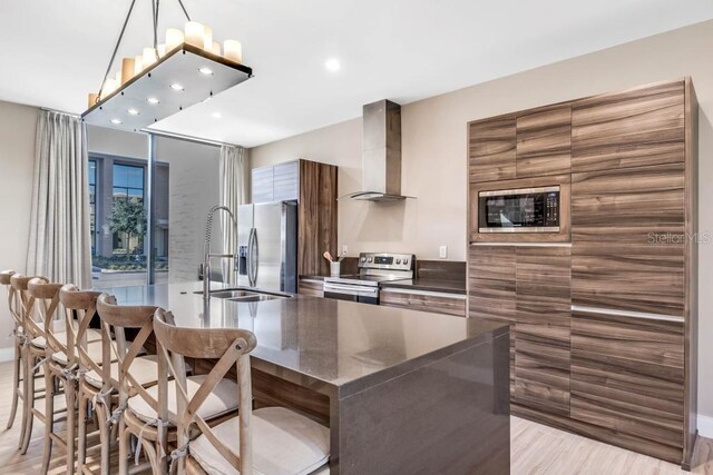 kitchen featuring a breakfast bar area, stainless steel appliances, wall chimney exhaust hood, dark countertops, and modern cabinets