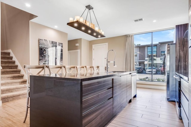 kitchen featuring a sink, light wood-style floors, white cabinets, a large island, and decorative light fixtures