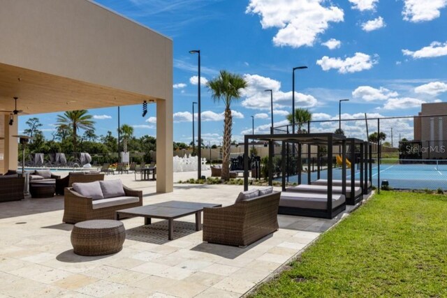 view of property's community featuring a patio area, a tennis court, fence, and an outdoor hangout area