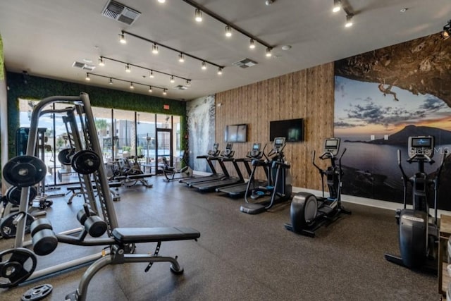 exercise room with rail lighting, visible vents, and wood walls