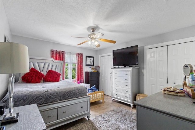 bedroom featuring dark wood-type flooring, ceiling fan, a textured ceiling, and two closets