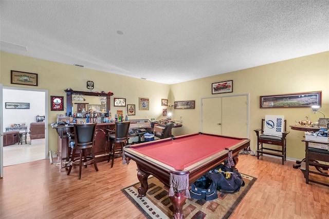 playroom featuring pool table, light wood finished floors, a bar, and a textured ceiling