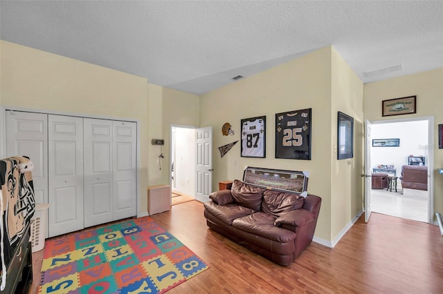 living area with a textured ceiling, baseboards, visible vents, and light wood-style floors