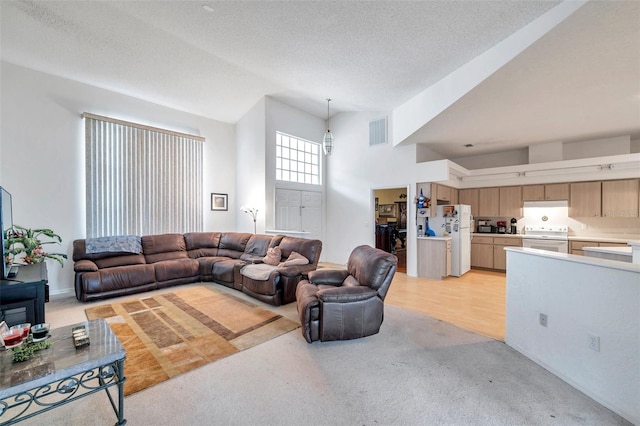 living area featuring light carpet, a high ceiling, visible vents, and a textured ceiling