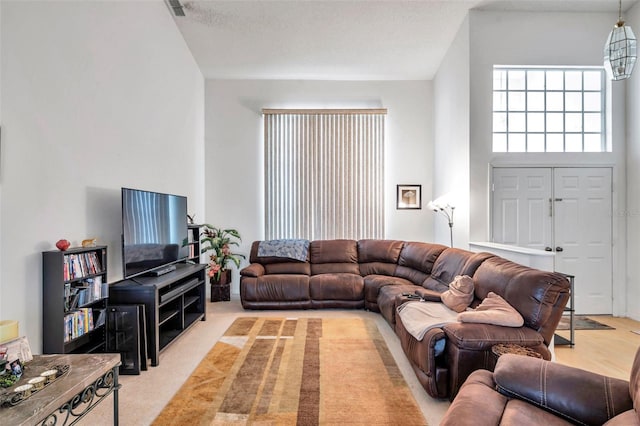 living room featuring light carpet, visible vents, a high ceiling, and a textured ceiling