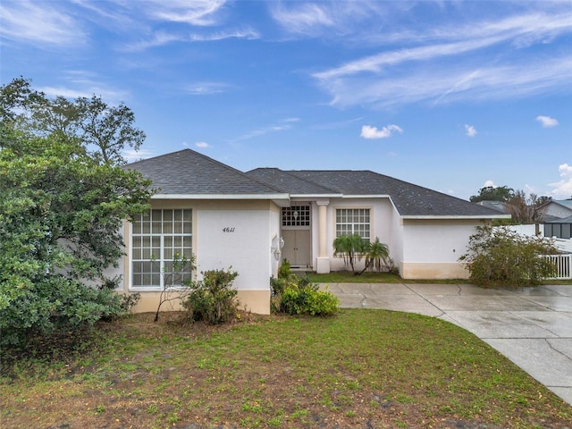 single story home featuring a front yard, roof with shingles, and stucco siding