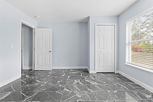 unfurnished bedroom with a closet, baseboards, and marble finish floor