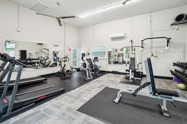 exercise room with concrete block wall, a textured ceiling, and an AC wall unit