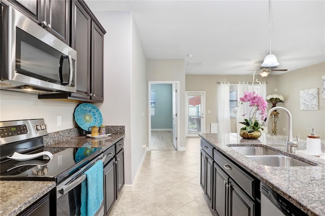 kitchen with light stone counters, a sink, a ceiling fan, dark brown cabinets, and appliances with stainless steel finishes