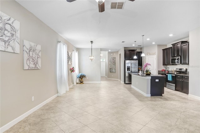 kitchen featuring pendant lighting, stainless steel appliances, dark countertops, visible vents, and a kitchen island with sink