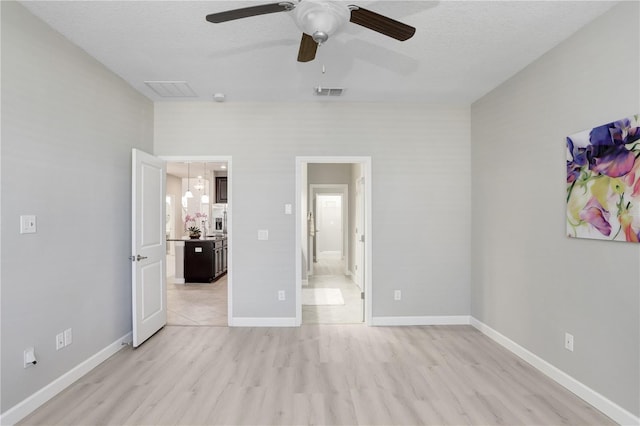 unfurnished bedroom with visible vents, light wood-style flooring, connected bathroom, a textured ceiling, and baseboards