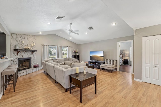 living area featuring vaulted ceiling, a stone fireplace, light wood-style flooring, and visible vents