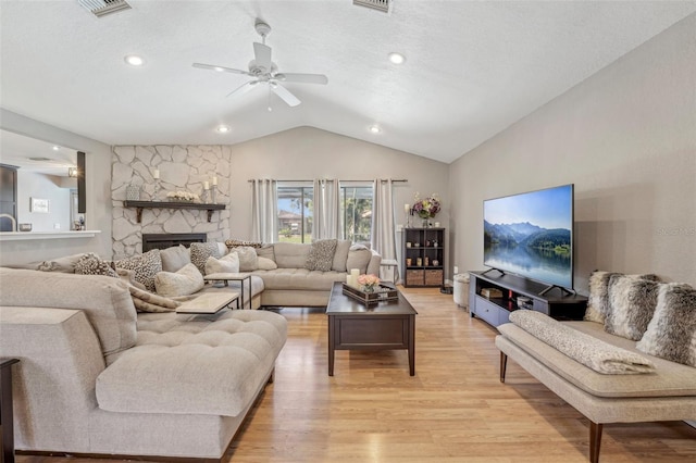 living area with a textured ceiling, a stone fireplace, visible vents, vaulted ceiling, and light wood-type flooring