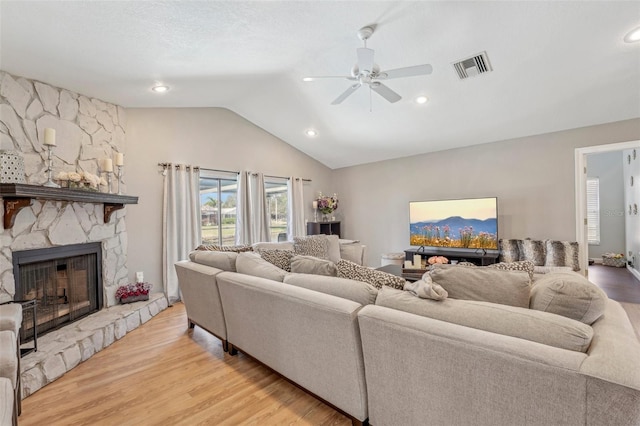 living area featuring a fireplace, visible vents, light wood-style floors, vaulted ceiling, and ceiling fan