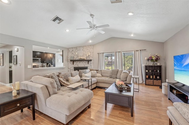 living room with lofted ceiling, light wood-type flooring, visible vents, and a textured ceiling