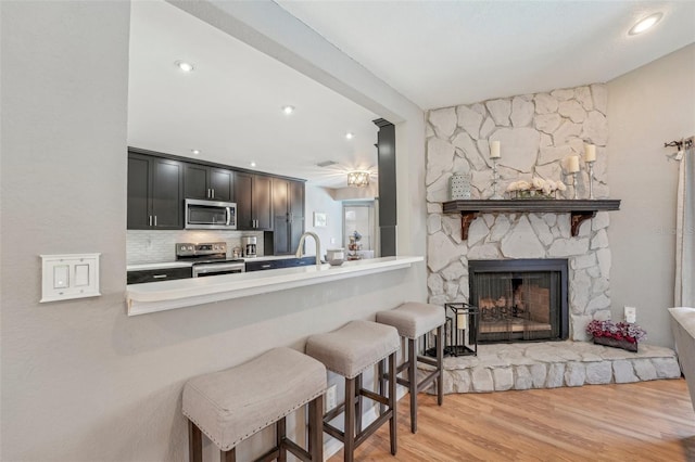 kitchen featuring light wood finished floors, a breakfast bar area, a peninsula, stainless steel appliances, and light countertops