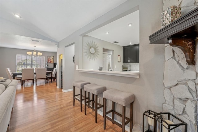 kitchen featuring light wood finished floors, light countertops, vaulted ceiling, a peninsula, and a kitchen bar