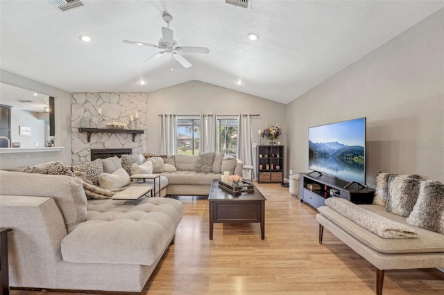 living room with visible vents, ceiling fan, a fireplace, light wood finished floors, and lofted ceiling