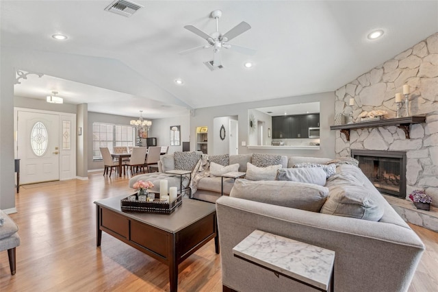 living area featuring visible vents, ceiling fan with notable chandelier, a stone fireplace, and lofted ceiling