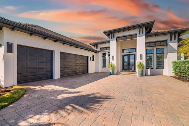 view of front of home featuring a garage, french doors, decorative driveway, and stucco siding