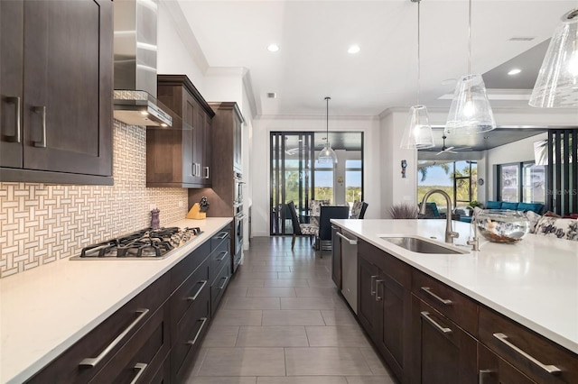 kitchen featuring light countertops, wall chimney range hood, appliances with stainless steel finishes, and pendant lighting