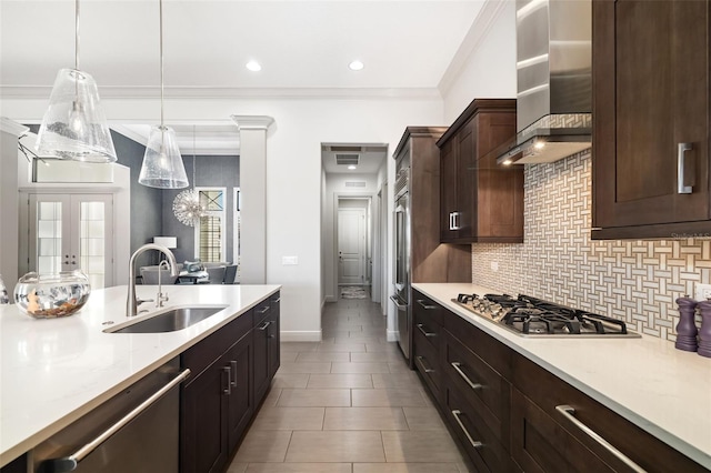 kitchen featuring wall chimney exhaust hood, appliances with stainless steel finishes, hanging light fixtures, crown molding, and a sink