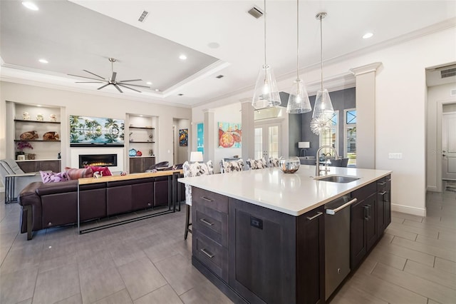 kitchen with open floor plan, light countertops, hanging light fixtures, stainless steel dishwasher, and an island with sink