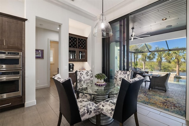 dining room with ceiling fan, light tile patterned flooring, baseboards, ornamental molding, and a dry bar