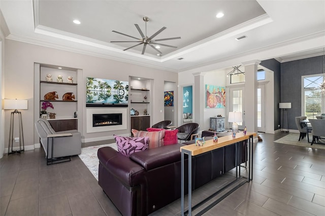 living area with built in features, decorative columns, a raised ceiling, visible vents, and a glass covered fireplace