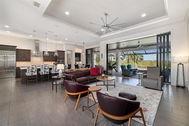 living area featuring visible vents, a raised ceiling, and a ceiling fan