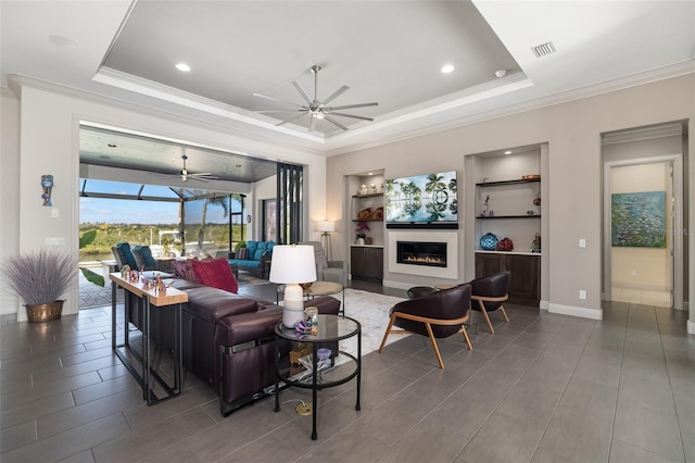 living area featuring a sunroom, a raised ceiling, a glass covered fireplace, and a ceiling fan