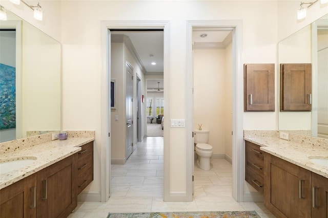 bathroom featuring ornamental molding, two vanities, a sink, and toilet