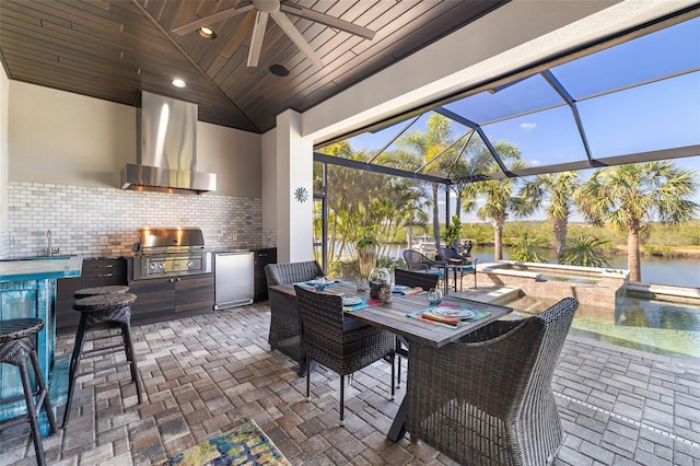 view of patio / terrace with an outdoor kitchen, a lanai, an in ground hot tub, a water view, and a grill