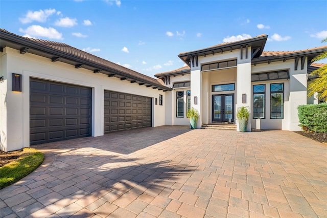 view of front of house featuring an attached garage, stucco siding, decorative driveway, and french doors