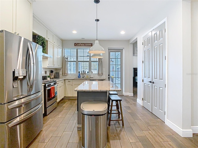 kitchen featuring wood finish floors, tasteful backsplash, a center island, white cabinetry, and appliances with stainless steel finishes