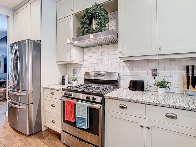 kitchen featuring light wood-style flooring, appliances with stainless steel finishes, wall chimney exhaust hood, decorative backsplash, and light stone countertops