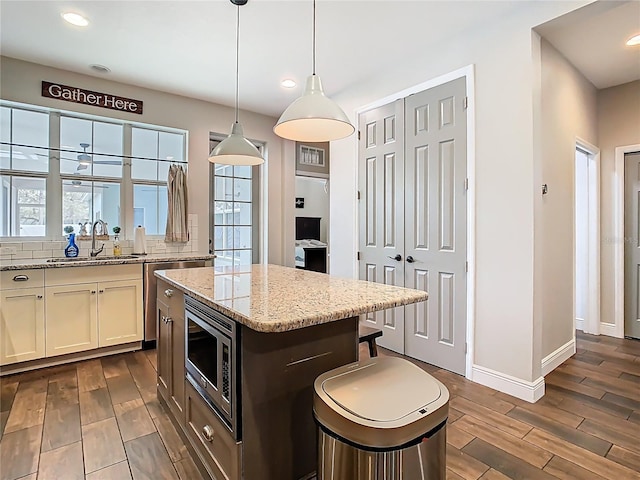 kitchen featuring stainless steel microwave, light stone counters, wood tiled floor, and a sink