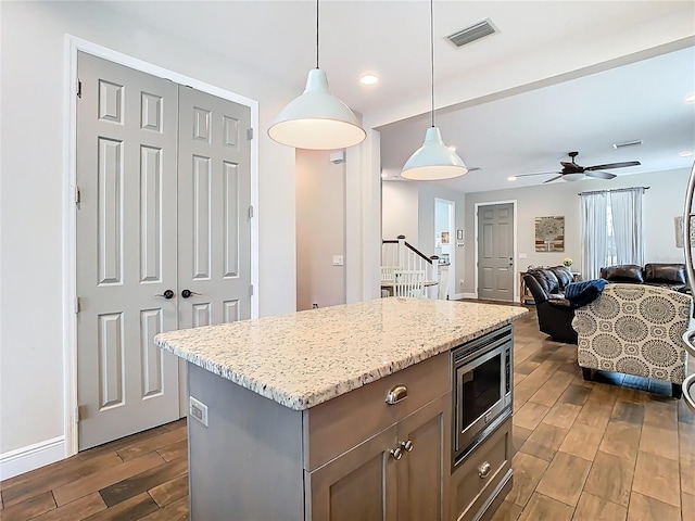 kitchen with visible vents, a kitchen island, wood tiled floor, hanging light fixtures, and stainless steel microwave