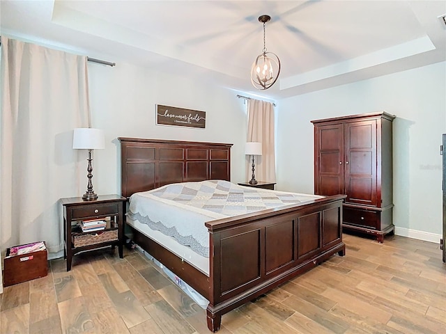 bedroom with visible vents, baseboards, a chandelier, light wood-style floors, and a raised ceiling