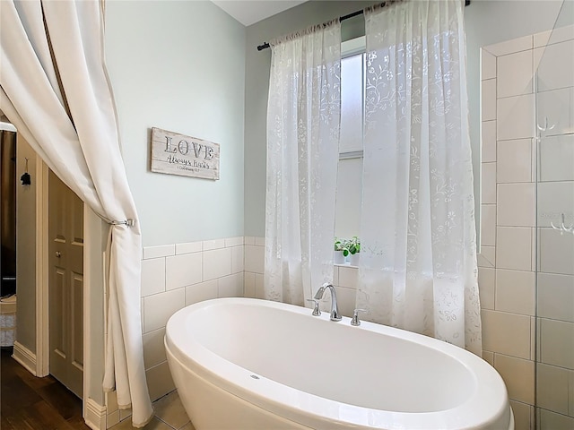 full bath featuring a freestanding bath, tile walls, and wood finished floors