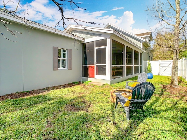 rear view of house featuring a yard, a sunroom, stucco siding, and fence