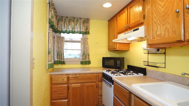 kitchen with white gas range, light countertops, under cabinet range hood, black microwave, and a sink