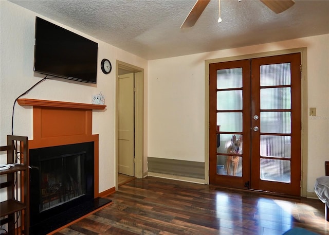 unfurnished living room featuring a fireplace with raised hearth, a textured ceiling, a ceiling fan, french doors, and dark wood-style floors