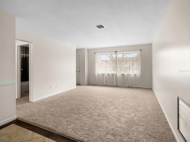 spare room featuring a textured ceiling, carpet floors, visible vents, and baseboards