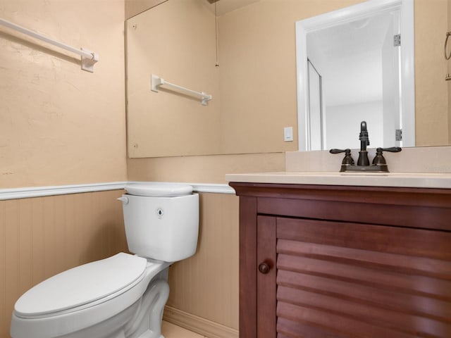 half bathroom featuring toilet, a wainscoted wall, and vanity