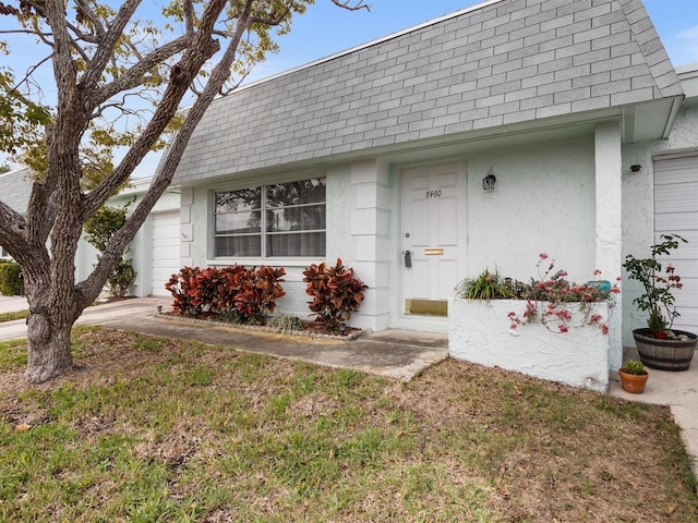 view of front of house featuring a shingled roof, a front lawn, mansard roof, and stucco siding