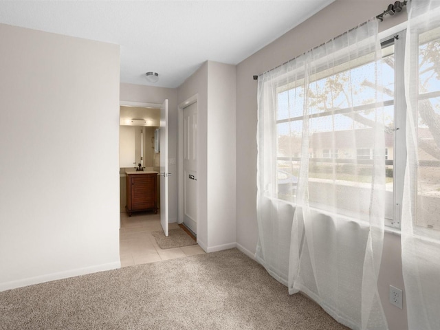 unfurnished bedroom with light carpet, ensuite bath, baseboards, and light tile patterned flooring