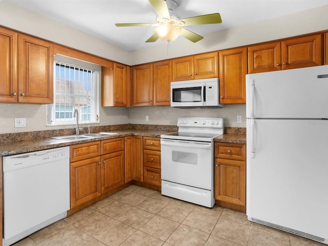 kitchen with white appliances, brown cabinetry, dark countertops, and a sink