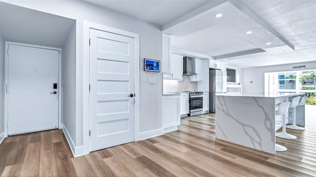 855 Bayway Blvd Unit 105, Clearwater, FL 33767 - kitchen featuring stainless steel appliances, a breakfast bar area, light wood-style floors, white cabinetry, and wall chimney range hood