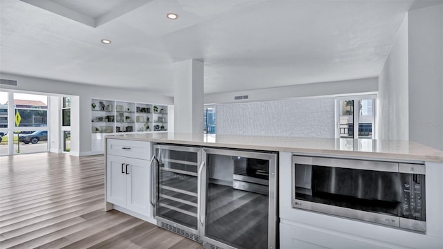 855 Bayway Blvd Unit 105, Clearwater, FL 33767 - kitchen featuring stainless steel microwave, open floor plan, light wood-style flooring, wine cooler, and white cabinets